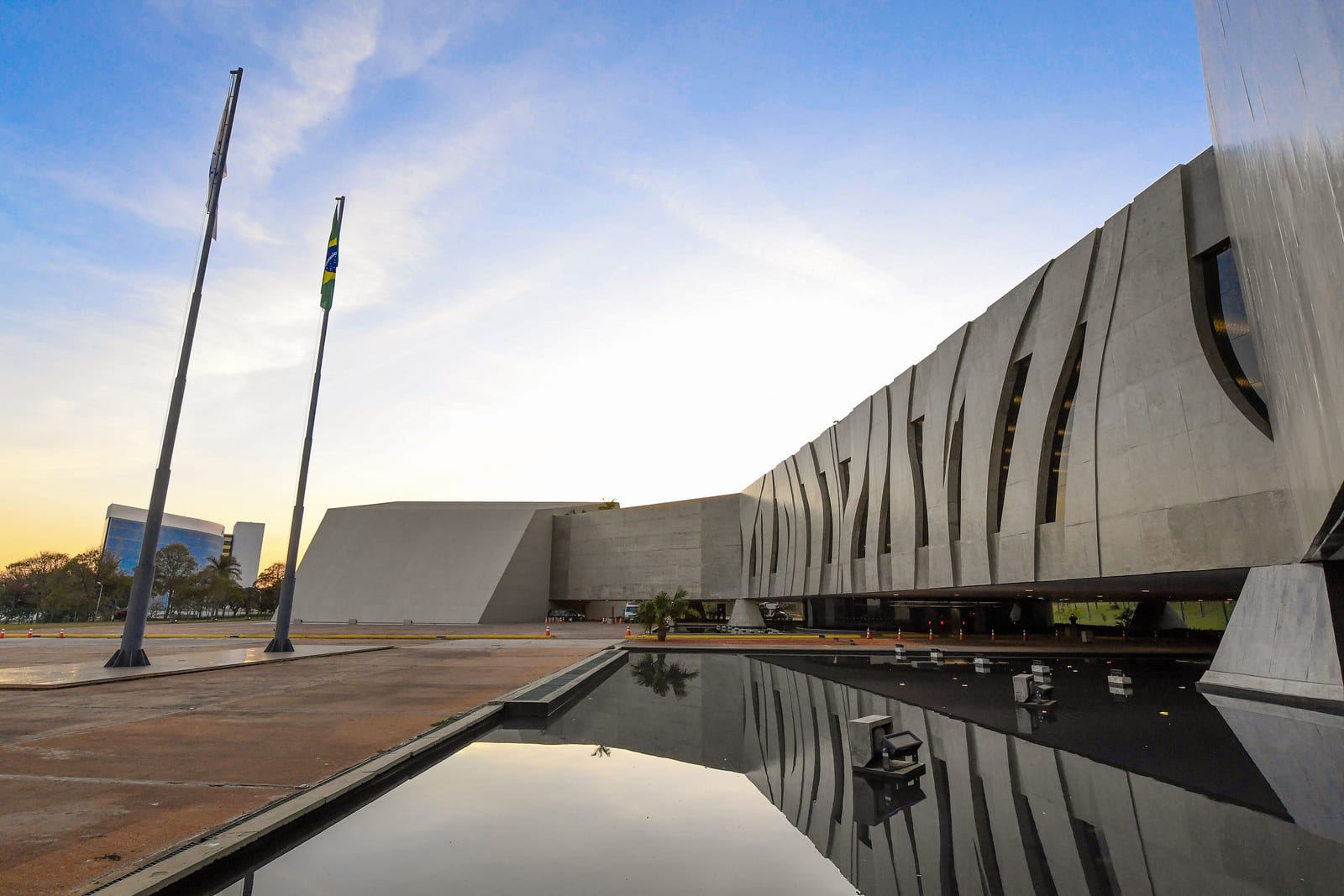 Sede do Superior Tribunal de Justiça, em Brasília, ao fim da tarde, com a fachada de aletas refletida no espelho d'água e dois mastros à esquerda