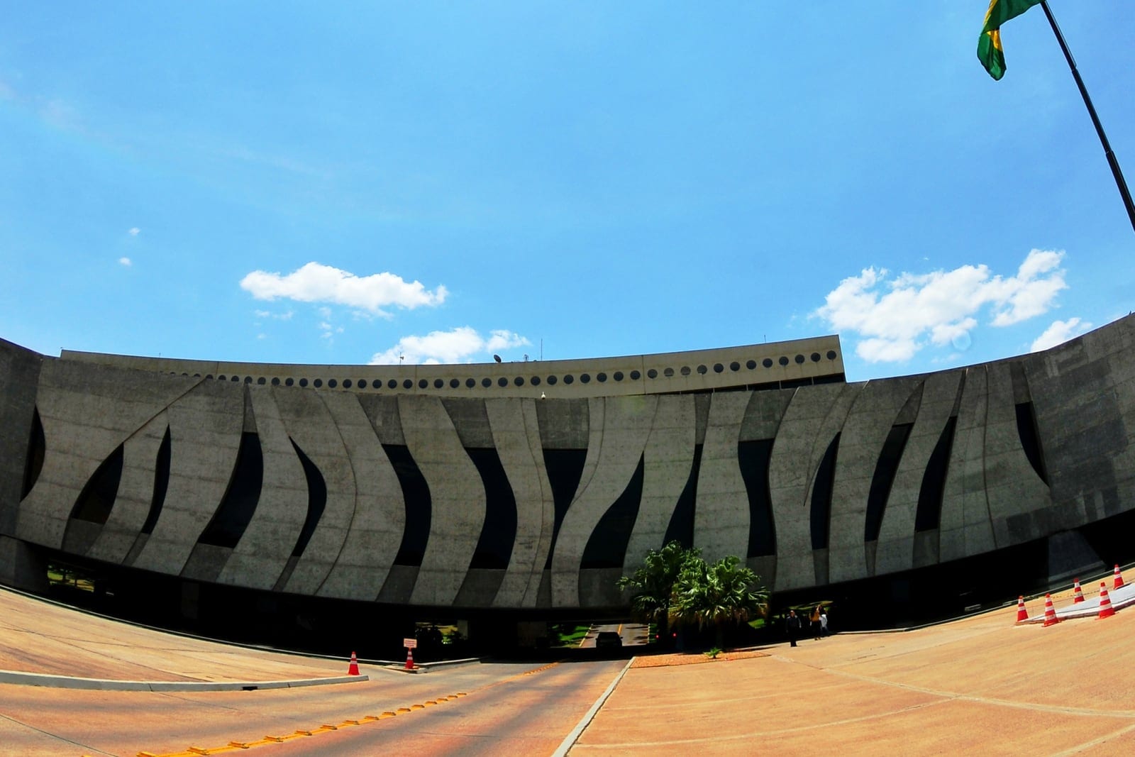 Fachada curva da sede do Superior Tribunal de Justiça, em Brasília, sob céu azul, com a bandeira do Brasil