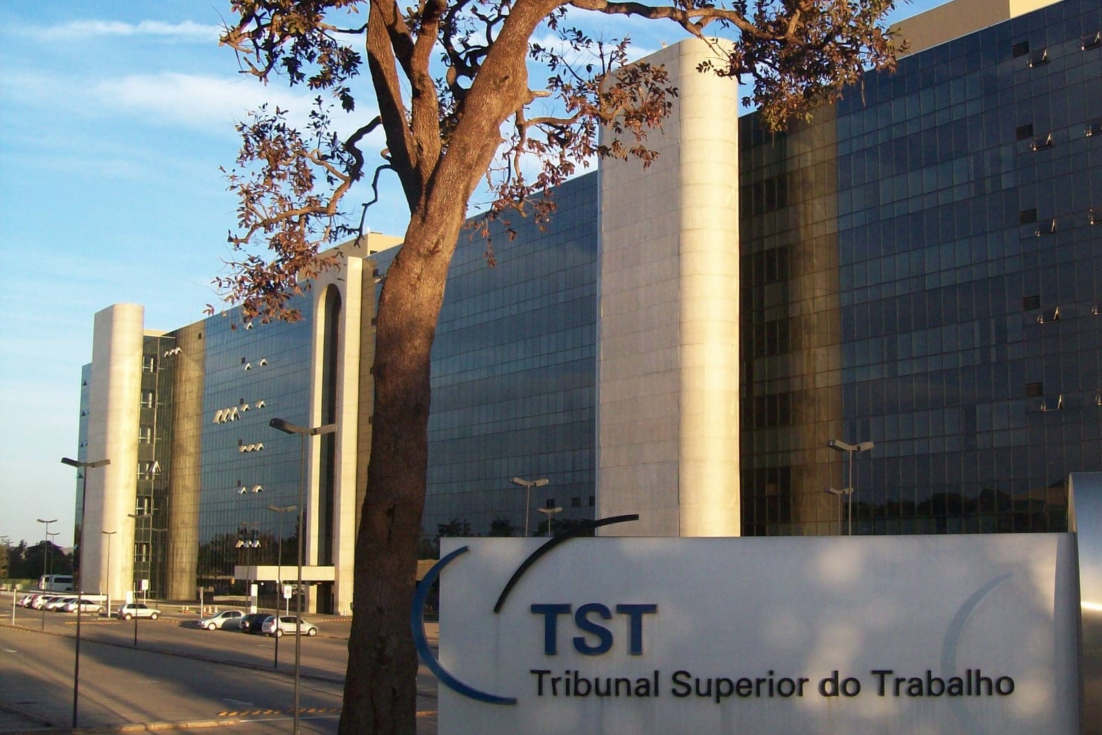 Sede do Tribunal Superior do Trabalho, em Brasília, com a placa do tribunal e uma árvore em primeiro plano